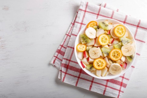 Vegetarian salad of bananas, apples, pears, kumquats and kiwi on linen tablecloth, top view, flat