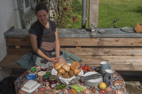 Young mum with baby in a sling at the breakfast table on the terrace, Mecklenburg-Vorpommern,