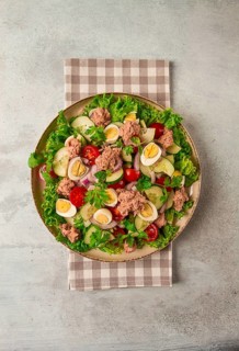 Tuna salad, vegetable salad with quail eggs, lettuce, red onion and cucumbers, on a light gray