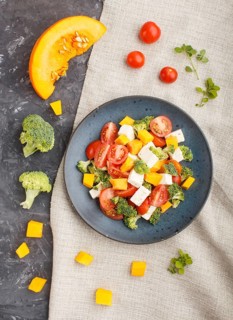 Vegetarian salad with broccoli, tomatoes, feta cheese, and pumpkin on a blue ceramic plate on a