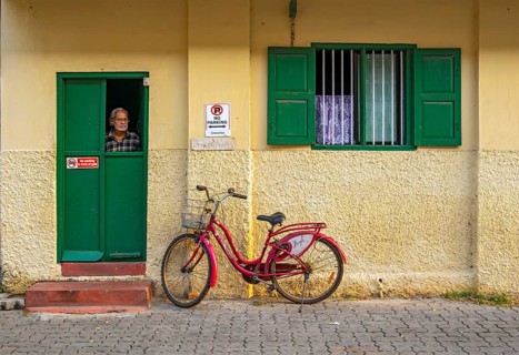 Man looks out a window of yellow house with red bicycle, Fort Kochi, Cochin, Kerala, India, Asia