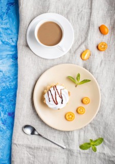Cake with whipped egg cream on a light brown plate with kumquat slices and mint leaves on a blue