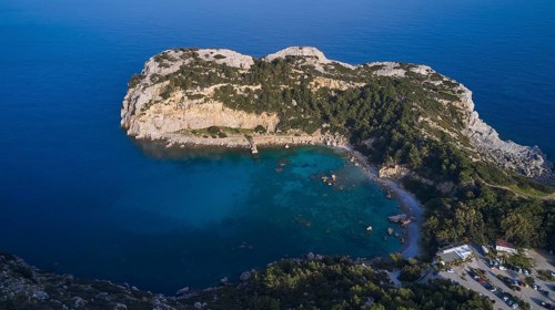 Aerial view of a green, peaceful bay with clear water, steep cliffs and far-reaching ocean under a