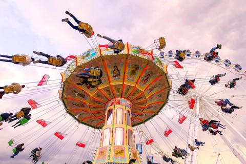 Chain carousel in motion with cheerful people in front of a cloudy sky, Ferris wheel, wave flight,