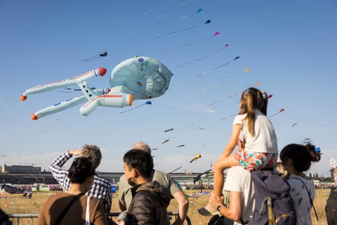 Visitors watch flying kites, including in the shape of the USS Enterprise, in front of the Berlin