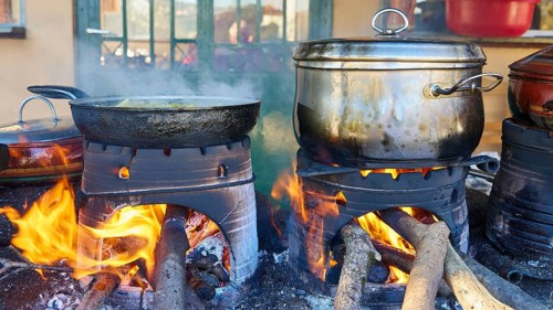 Several pots and pans cooking on open fires in a rustic kitchen, flames flickering on the logs,