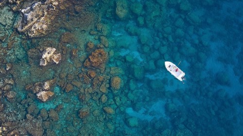 Drone shot, boat in crystal clear blue water between rocks and corals, Anthony Quinn Bay, Vagies