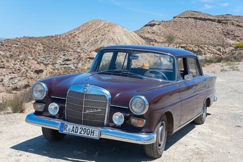 Brown Mercedes-Benz W110 classic car in the desert with sand and blue sky in the background, shiny