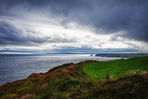 Dramatic coastal landscape with cloudy skies and green meadows bordering the cliffs, Waterford