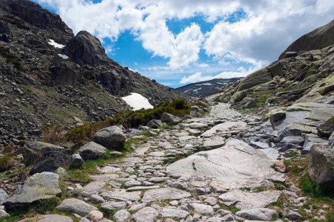 A stony path winds its way through a rocky mountain landscape under a cloudy sky, hiking area,