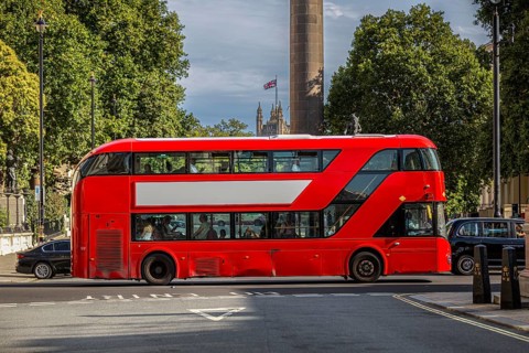 A red double-decker bus with a free advertising space or banner drives through a tree-lined street