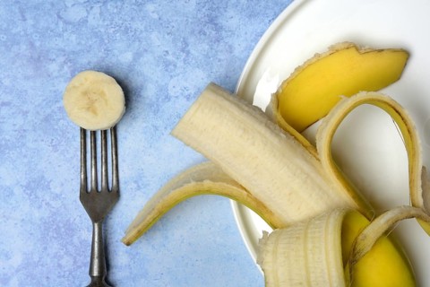 Opened banana on plate and fork with banana slice