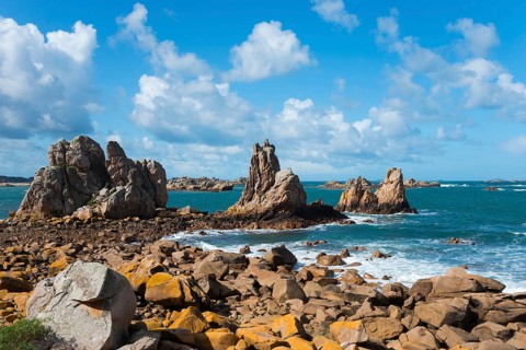 Rocky coastal landscape with crashing waves and a clear blue sky with light clouds, Plage de Pors