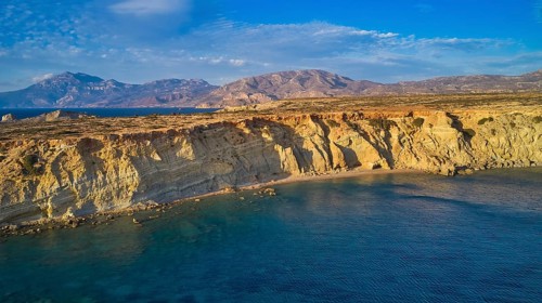 Coastal landscape with calm water and rocky cliffs under blue sky, drone shot, evening light,