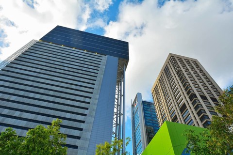 Modern skyscrapers with a backdrop of a blue sky and scattered clouds, surrounded by trees and