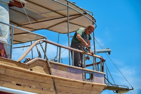 A man renovates a wooden boat in the dry dock on a sunny day, Patmos Marine, boatyard, Diakofti,