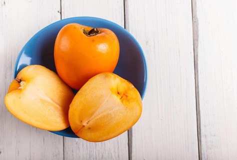 Ripe orange persimmon in a blue plate on white wooden background, with copy space