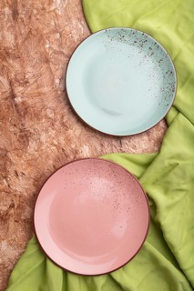 Two empty blue and pink plates on brown concrete background and green textile. Top view, close up,