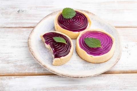 Sweet tartlets with jelly and milk cream on a white wooden background. Side view, close up