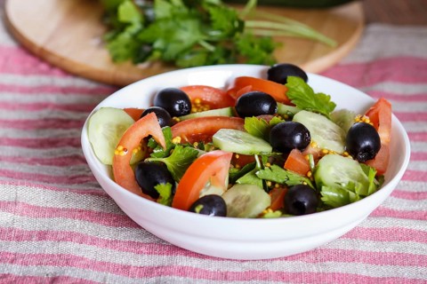 Vegetarian salad of tomatoes, cucumbers, parsley, olives and mustard on linen tablecloth, close up,