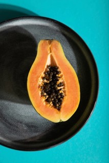 Ripe cut papaya on gray plate on blue pastel background. Top view, flat lay, close up, hard light.