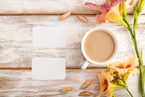 White paper business card mockup with orange day-lily flower and cup of coffee on white wooden