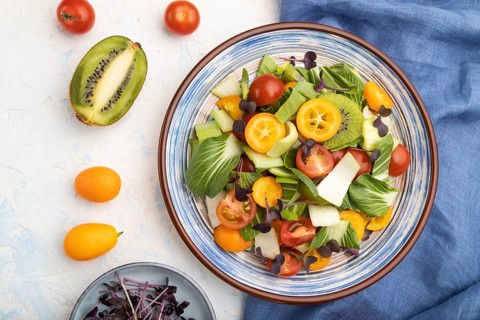 Vegetarian salad of pac choi cabbage, kiwi, tomatoes, kumquat, microgreen sprouts on a white