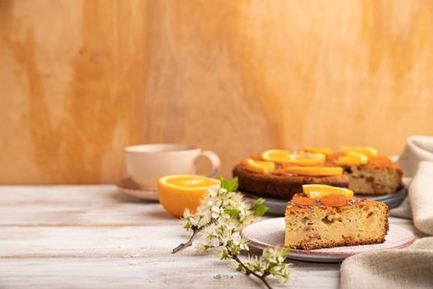 Orange cake and a cup of coffee on a white wooden background and linen textile. Side view, copy