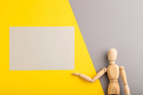 Wooden mannequin holding gray blank poster on gray and yellow pastel background. copy space,