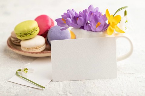 White paper business card mockup with spring snowdrop crocus flowers and multicolored macaroons on