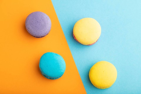 Yellow, purple and blue macaroons on blue and orange pastel background. top view, copy space, close