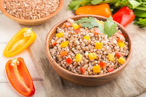 Buckwheat porridge with vegetables in wooden bowl on a white wooden background and linen textile.