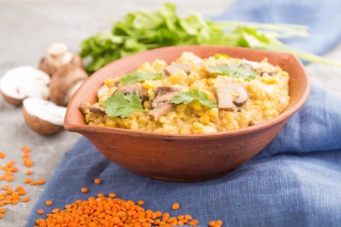 Lentils porridge with champignons and coriander in a clay bowl on a gray concrete background and