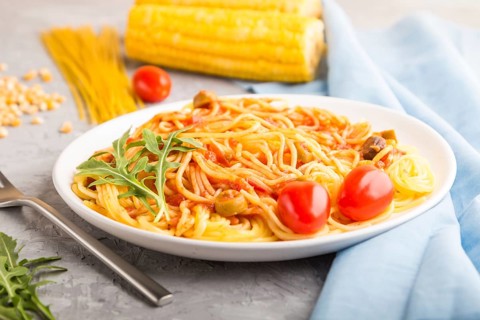 Corn noodles with tomato sauce and arugula on a gray concrete background and blue textile. Side