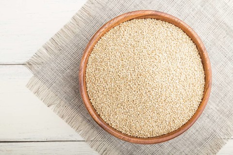 Wooden bowl with raw white quinoa seeds on a white wooden background and linen textile. Top view,