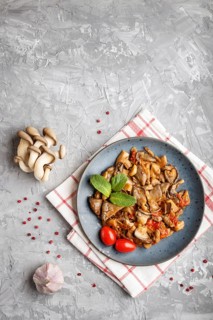 Fried oyster mushrooms with tomatoes on gray concrete background. Top view, copy space
