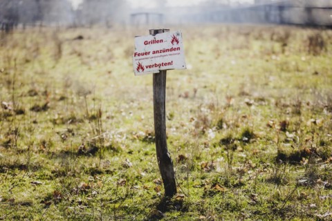 A sign with the inscription 'Barbecues and lighting fires prohibited' stands in a meadow in Berlin,