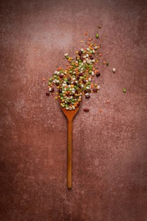 Wooden spoon, with an assortment of legumes, beans, peas, top view, on a brown background