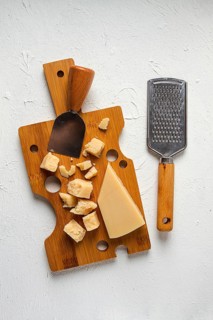 Hard cheese, parmesan, on a cutting board, cheese knife, grater, top view, no people