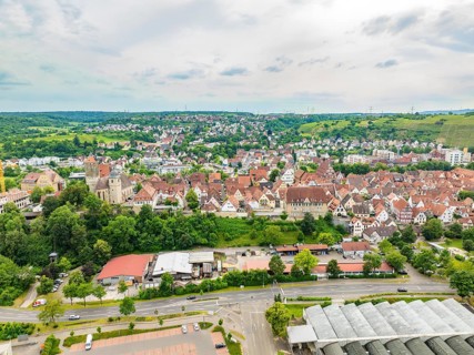 Overview of a town with red tiled roofs, embedded in hilly, green landscapes, crossed by various