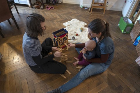 Young mother with her sister and with her son, 8 months, playing on the parquet floor,