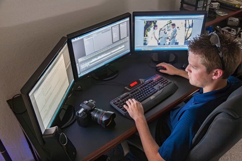 Young adult male videographer editing a wedding video on his computer system