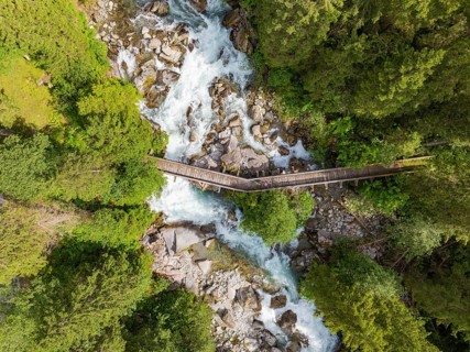Aerial view of a wooden bridge over a raging river, surrounded by dense forest, Zillertal, Austria,