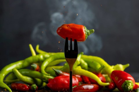A red pepperoni on a fork, pepperoni and some smoke in the background, food photography