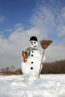 Decorated snowman with carrot nose, hat, pipe, scarf and broom in the snow in winter