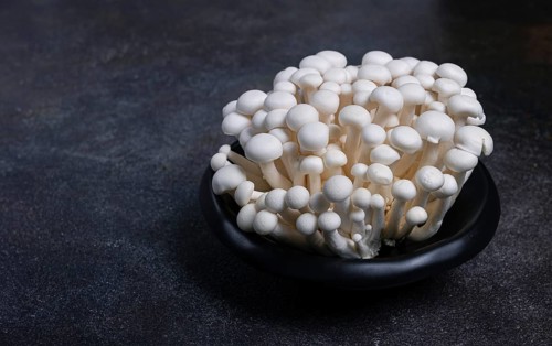 Fresh white shimeji mushrooms, on a black plate, no people.
