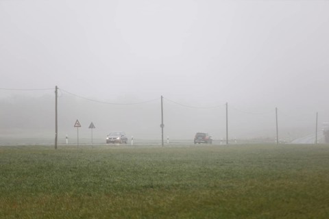 Cars drive over a country road with their lights on in dense fog, Neugarten, Brandenburg, 06.11