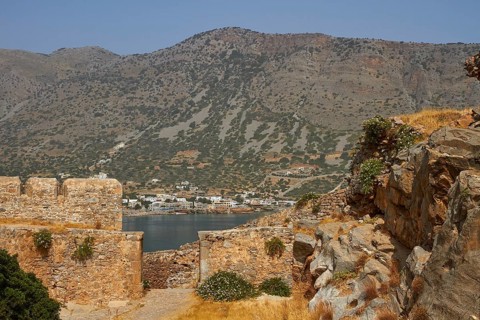 The remains of ancient stone structures in front of a mountainous landscape with a nearby village,