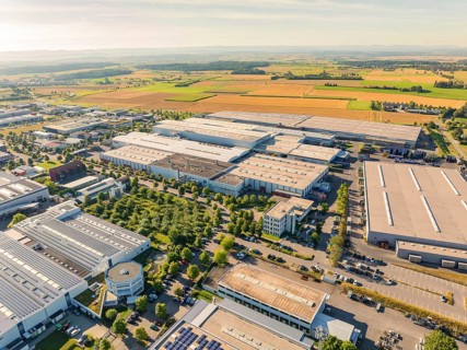 Industrial area with several large buildings, surrounded by green fields and trees, a bright and