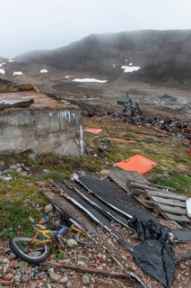 Broken children's bicycle, pallets, plywood, junkyard in rocky, hilly landscape with snow remains,